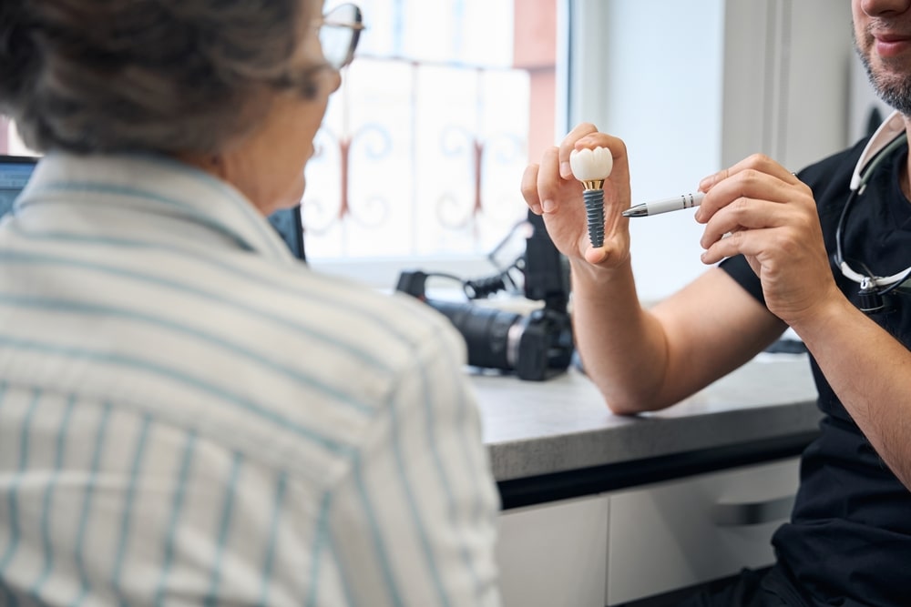 Un dentiste montre un modèle d'implantologie représentant une couronne sur implant